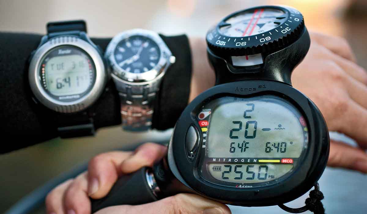 Right hand holds a dive computer and in background is a left wrist with two watches