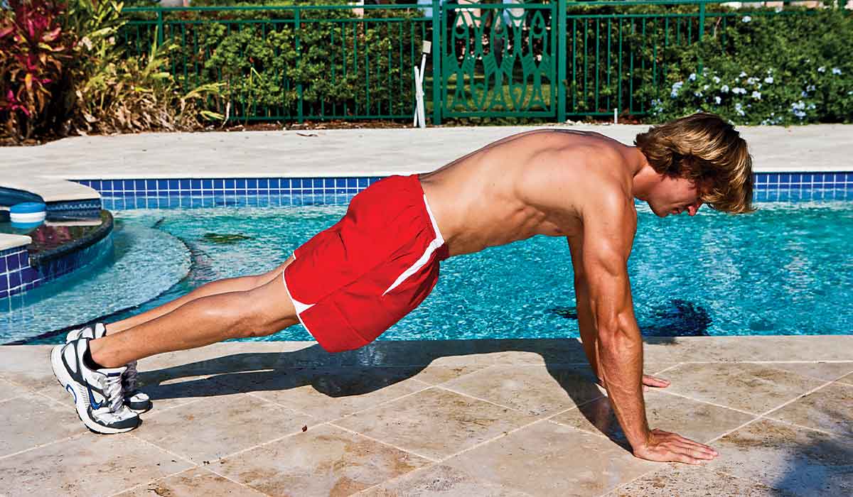 Shirtless man in red shorts holds a plank position