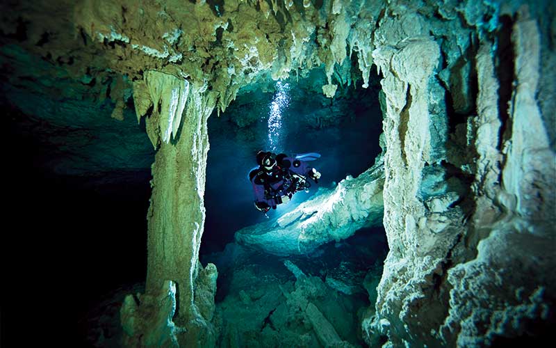 Single diver swims through a dark cave