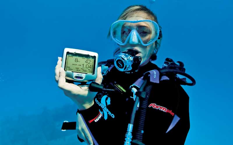 Submerged female diver holds up dive computer