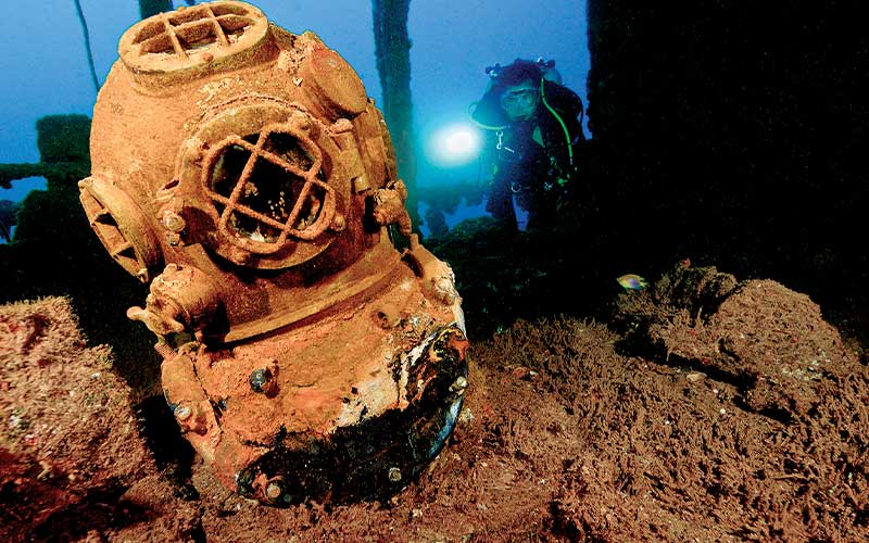 Sunken antique diver helmet with a diver in the background