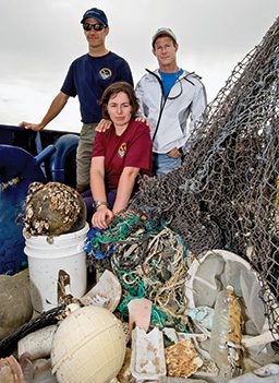 Two men and one woman pose next to a giant pile of garbage