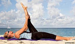 Woman lies on purple towel with left leg extended to the sky