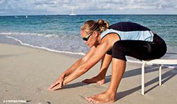 Woman sits on chair and is hunched over, reaching as far as she can