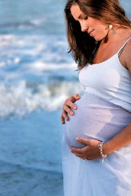 Woman stands on beach and holds pregnant belly