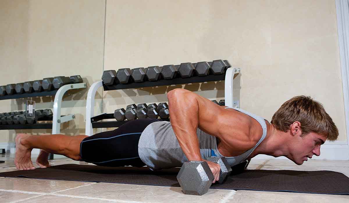 Barefoot man in a gray tank top performs a dumbbell push-up
