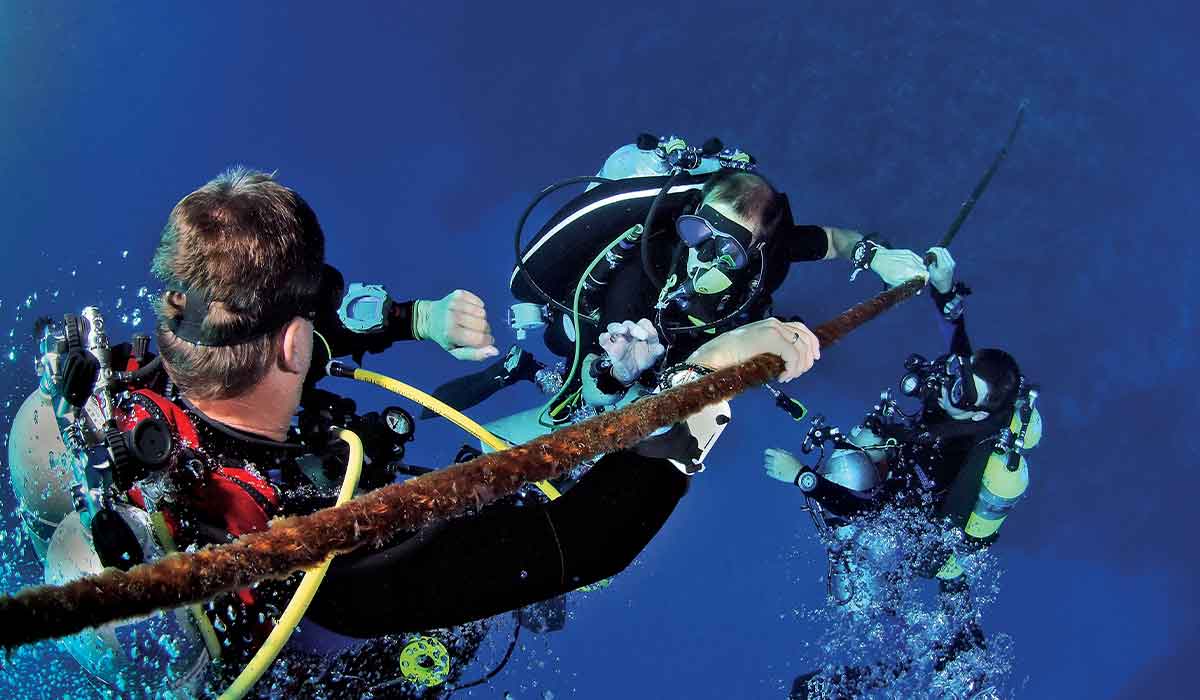 Three divers pause on a mooring line for a stop during their ascent