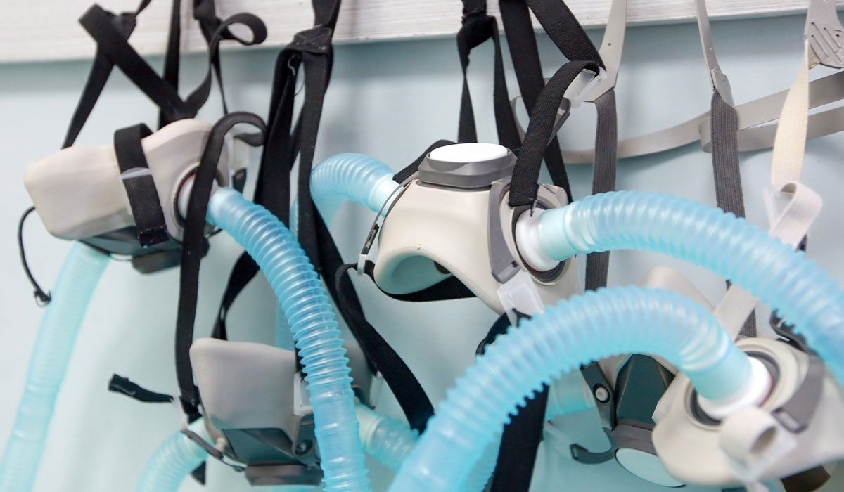 Several hyperbaric masks with blue tubes hang outside a chamber and wait use