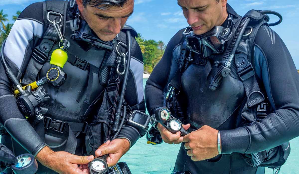 Two male divers stand in tropical shore and check their gear
