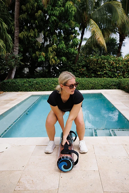 Woman starts the upswing press with feet shoulder-width apart and the bag between her legs, with the back of the bag by her heels.