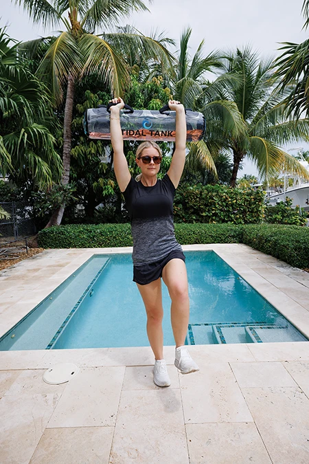 Woman brings chest up as she curls the bag. She simultaneously drives her left leg up and presses the bag over her head.