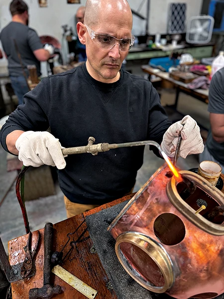 Nelson uses a torch to solder a part onto a copper helmet