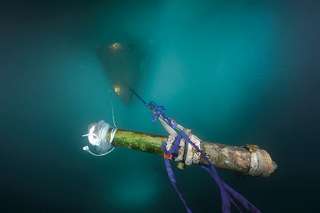 A cannon is hoisted toward the surface during an early on-ice artifact recovery operation in the Arctic