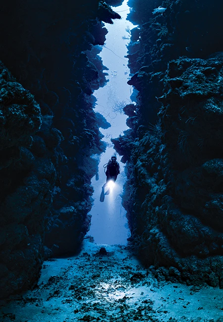 A diver swims through a narrow split in the reef at Calvin's Crack