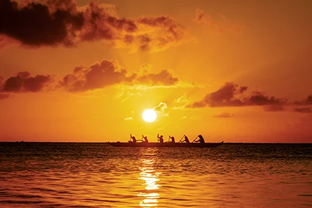 As the sun sinks toward
the horizon, paddlers drive a traditional outrigger canoe