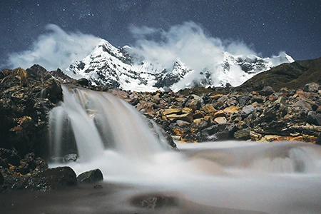Fringed in clouds against the night sky, Nevado Ausangate, the highest mountain in the Andes of southern Peru, looms above a glacial melt waterfall.